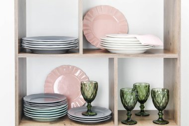 Beyaz duvarın yanında farklı plakalar ve gözlüklerle raf ünitesi.