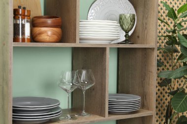 İçerideki yeşil duvarın yanında farklı bulaşık takımları ve gözlüklerle raf ünitesi.