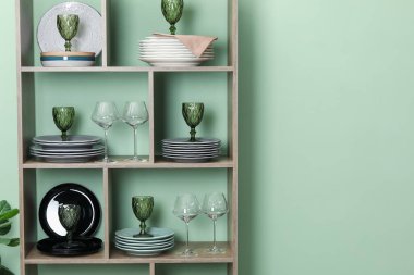 Kapalı alanda yeşil duvarın yanında farklı plaka ve gözlüklerle raf ünitesi, metin için yer