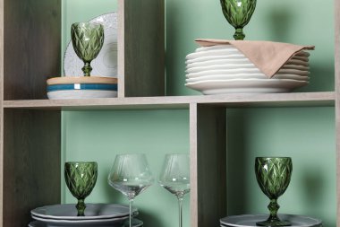 Kapalı alandaki yeşil duvarın yanında farklı plaka ve gözlüklerle raf ünitesi.