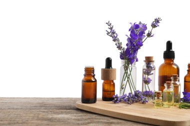 Beyaz arka plana karşı ahşap masa üzerinde gerekli yağlar ve farklı bitkiler.