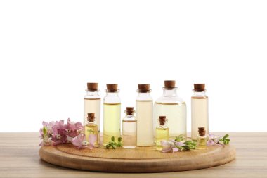 Beyaz arka plana karşı ahşap masa üzerinde gerekli yağlar ve farklı bitkiler.