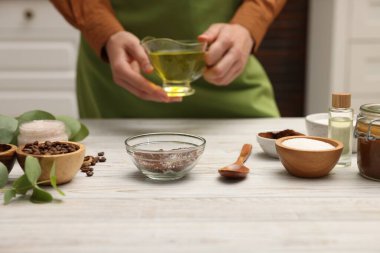 Doğal temizlik yapıyorum. Beyaz ahşap masada kaseye yağ koyan kadın, yakın plan.