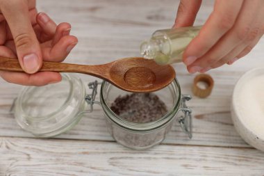 Doğal temizlik yapıyorum. Beyaz ahşap masada kavanoza gerekli yağı koyan kadın, yakın plan.