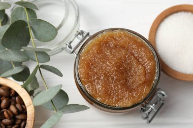 Cam kavanozda doğal vücut fırçası ve beyaz ahşap masa üzerindeki malzemeler.