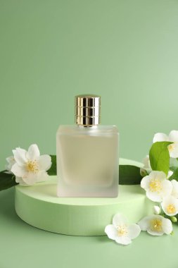 Yeşil arka planda bir şişe parfüm ve yasemin çiçeği. Metin için boşluk