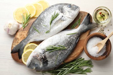 Taze çiğ dorado balığı, limon dilimleri, biberiye ve baharatlar beyaz ahşap masa, düz yatak. Organik deniz ürünleri