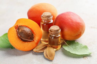 Açık gri masada gerekli yağ şişeleri, taze kayısılar, çekirdekler ve yeşil yapraklar, yakın plan.