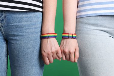 LGBT konsepti. Gökkuşağı bileklikli kadınlar yeşil arka planda el ele tutuşuyorlar, yakın plan.
