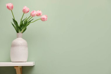 Açık yeşil duvarda pembe lalelerin olduğu beyaz raf, metin için boşluk.