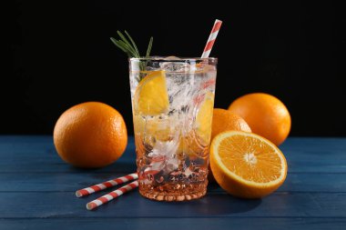 Bardakta portakallı maden suyu, mavi ahşap masada taze meyve ve pipetler, yakın plan.