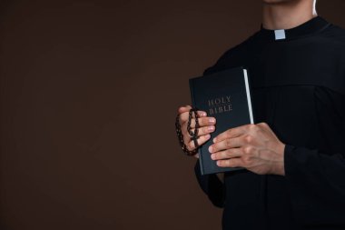 Kutsal İncil 'i ve kahverengi arka planda tespihi olan bir rahip, yakın plan. Metin için boşluk