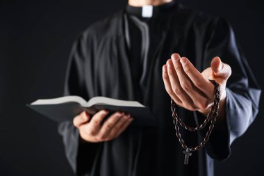 Kutsal İncil 'i olan ve siyah arka planda vaaz veren bir rahip, yakın plan.