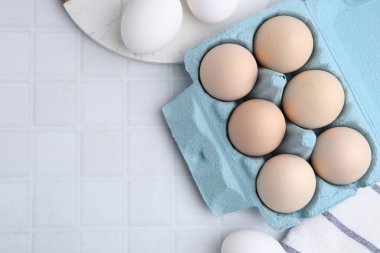 Yumurta kartonunda çiğ tavuk yumurtaları, beyaz fayanslı masa, düz yatak. Metin için boşluk