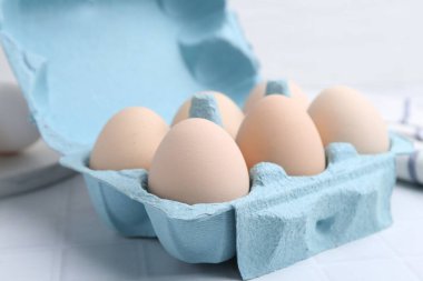 Yumurta kartonunda çiğ tavuk yumurtası, beyaz fayanslı masa, yakın plan.
