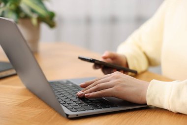 Kapalı alandaki ahşap masada dizüstü bilgisayar kullanan metin yazarı