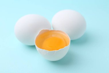 Açık mavi arka planda tam ve kırılmış tavuk yumurtaları, yakın plan.