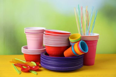 Bulanık arka plana karşı sarı ahşap masada tek kullanımlık plastik bulaşık takımı.