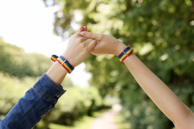 LGBT konsepti. Gökkuşağı bileklikli kadınlar dışarıda el ele tutuşuyorlar, yakın plan.