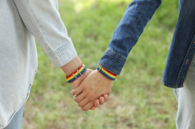 LGBT konsepti. Gökkuşağı bileklikli kadınlar dışarıda el ele tutuşuyorlar, yakın plan.