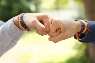 LGBT konsepti. Gökkuşağı bileklikli kadınlar açık havada yumruk tokuşturup yakınlaşırlar.