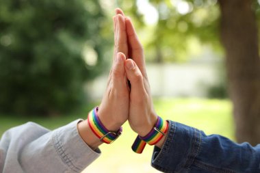 LGBT konsepti. Gökkuşağı bileklikli kadınlar dışarıda el ele tutuşuyorlar, yakın plan.