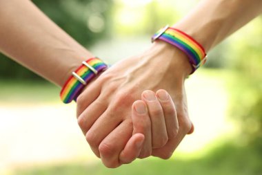 LGBT konsepti. Gökkuşağı bileklikli kadınlar dışarıda el ele tutuşuyorlar, yakın plan.