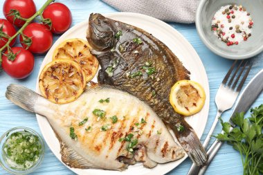 Açık mavi ahşap masada servis edilen limon dilimli ve otlu kızarmış balık. Ev yapımı deniz ürünleri yemeği.
