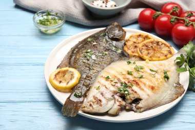 Lezzetli kavrulmuş balık, otlar, limon dilimleri ve açık mavi ahşap masa üzerinde domatesler, yakın plan. Ev yapımı deniz ürünleri yemeği.