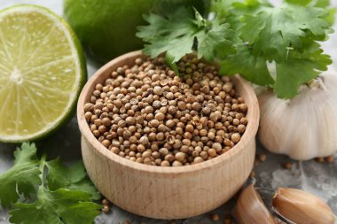 Kişniş tohumu, taze kişniş, kireç ve sarımsak gri desenli masa, yakın plan.