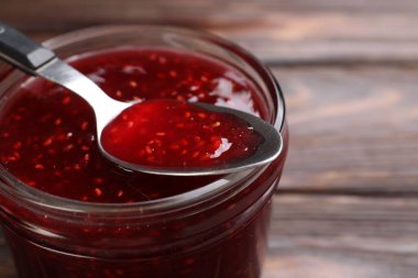 Cam kavanozda tatlı ahududu reçeli ve masada kaşık, yakın plan.