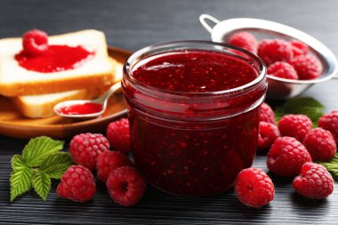 Tatlı ahududu reçeli cam kavanozda, böğürtlen ve ekmek dilimleri koyu gri ahşap masada, yakın plan