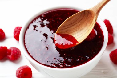 Beyaz masada kaseden kaşıkla ahududu reçeli alıp...