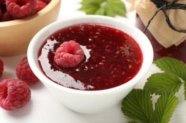 Tatlı ahududu reçeli, böğürtlen ve yeşil yapraklar beyaz ahşap masada, yakın plan