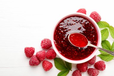 Tatlı ahududu reçeli kasede, böğürtlen ve yeşil yapraklar beyaz ahşap masada, düz yerde. Metin için boşluk