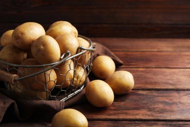 Bir sürü çiğ patates, metal sepet ve kahverengi bez, ahşap masanın üzerinde, yakın plan. Metin için boşluk