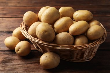 Tahta masada bir sürü çiğ patates ve hasır sepet, yakın plan.