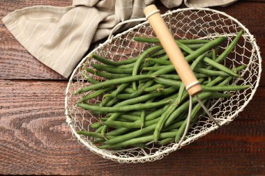 Beyaz sepet içinde taze bezelye kabukları ve ahşap masa üzerinde kumaş, üst görünüm