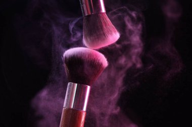 Siyah arkaplandaki neon ışıklarıyla göz farları renginde makyaj fırçaları, yakın plan