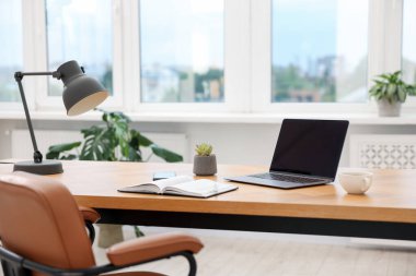 Modern dizüstü bilgisayarı ve ahşap masa üzerindeki kırtasiyesi olan şık bir iş yeri.