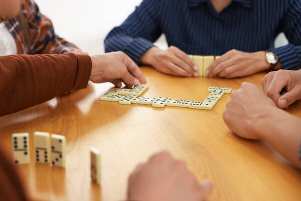 Друзья играют в домино за деревянным столом на светлом фоне, крупным планом