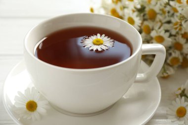 Fincanda Aromatik çay ve beyaz masada papatya çiçeği, yakın plan.