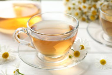 Cam fincanlarda romatik çay ve beyaz ahşap masada papatya çiçekleri, yakın plan.