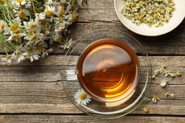 Cam bardakta Aromatik çay ve ahşap masada papatya çiçekleri.