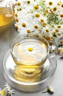 Lezzetli papatya çayı ve çiçekler gri masada, yakın plan.