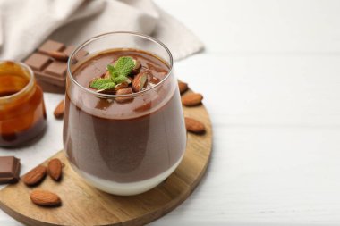 Bademli lezzetli çikolatalı panna cotta, beyaz ahşap masada nane ve karamel sosu, yakın plan. Metin için boşluk
