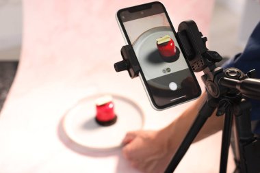 Adam stüdyodaki masada fotoşoplar için lezzetli tatlılarla kompozisyon hazırlıyor, akıllı telefon ve tripoda odaklanıyor. Profesyonel yemek fotoğrafçılığı.