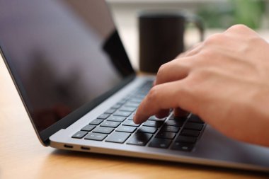 Kapalı alandaki ahşap masada dizüstü bilgisayar kullanan metin yazarı