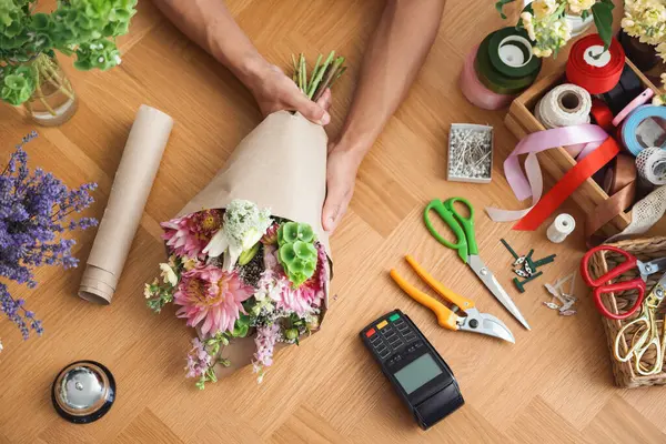 Ahşap masada çiçek buketi yapan profesyonel bir çiçekçi.