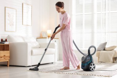 Kadın evinde elektrikli süpürgeyle halı temizliyor.